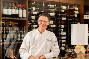 A Cater Dallas chef smiling in front of a wine cellar