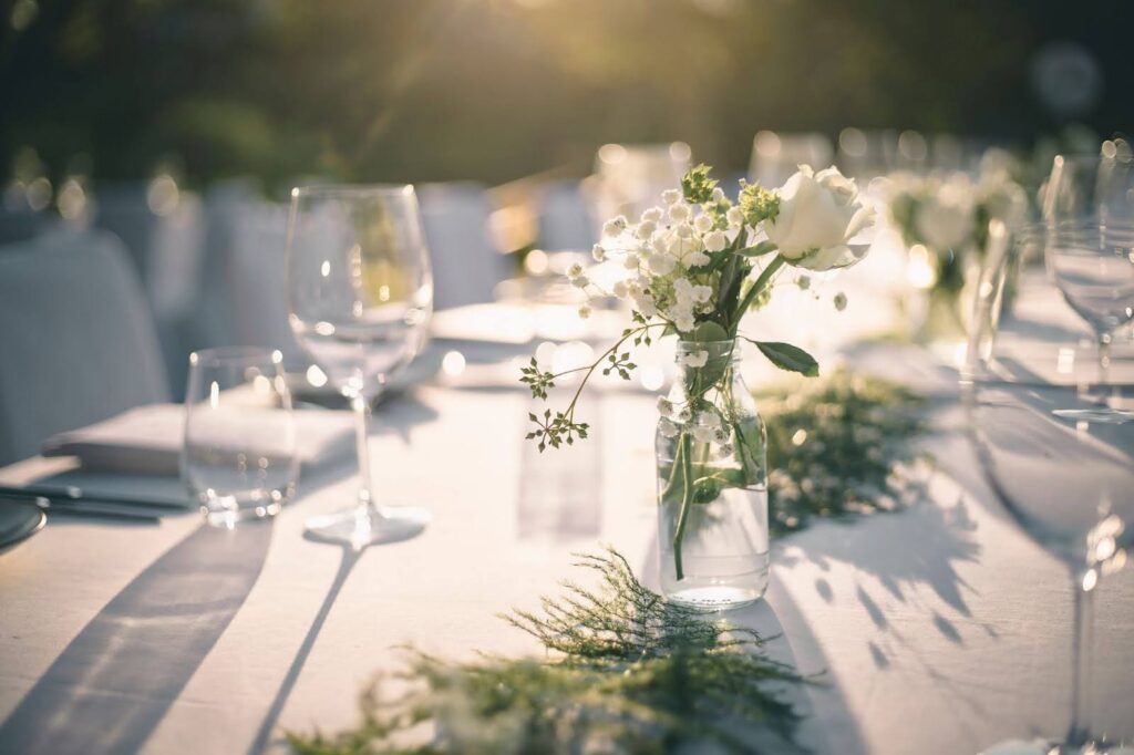 A wedding table setting with white linens and greenery