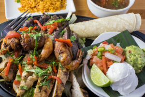 A tray of fijitas with a side of guac on a plated display