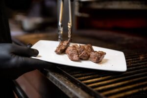 A photo of a chef pulling steak from a grill